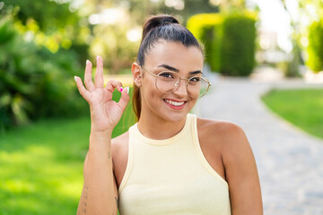 Wall Mural - Young pretty woman with glasses at outdoors showing ok sign with fingers