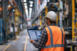 © Alberto Gonzalez  - Engineer in safety vest and hard hat working on a laptop in a modern industrial factory setting.