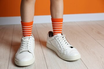 Wall Mural - Child wearing oversized sneakers near orange wall indoors, closeup. Space for text