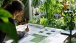 © Bhait - A landscape architect designing a garden with blueprints and plant samples, in a studio filled with natural light and greenery, Landscape design scene