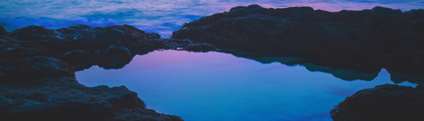 Poster - Small tidal pool with glowing rocks under a bright sky and serene waves