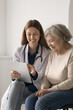 © fizkes - Modern tech in medicare. Vertical shot smiling aged female patient visit doctor look on pad pc screen in medic hands get consultation discuss lab test results in personal account on e-health platform