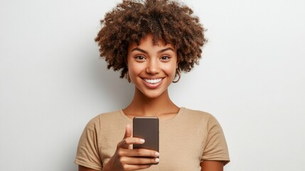 Wall Mural - A young woman with slightly curly short hair holds a smartphone in one hand and gives a thumbs-up with the other, her confident face radiating a happy smile