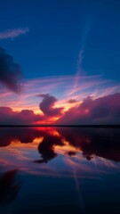 Fototapete - A beautiful sunset over a lake with mountains in the background. The sky is filled with clouds and the sun is setting
