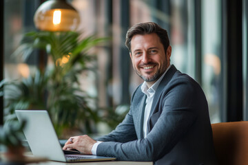 Poster - man is sitting at a table with a laptop in front of him. He is smiling and he is happy