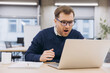 © anatoliycherkas - Professional businessperson expressing wide eyed surprise, reading shocking digital content while sitting at sleek workstation
