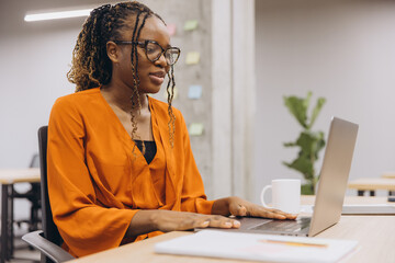 Wall Mural - Professional African American businesswoman focused on her laptop in a modern office setting, showcasing productivity and concentration