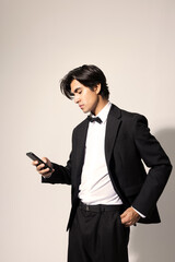 Handsome young man wearing elegant black suit and using smart phone posing over white background. Isolated.