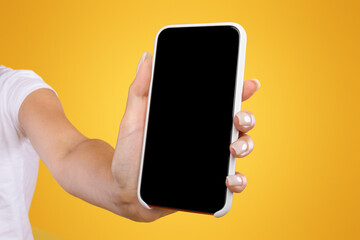 Poster - Trendy Mobile Phone. Closeup of female holding smartphone with black empty screen in hand, showing device close to camera. Gadget with blank space, mock up, selective focus, orange blurred background