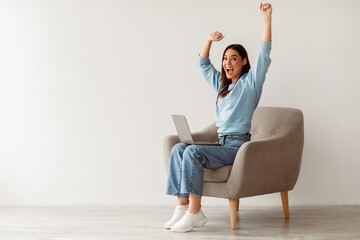 Poster - Full length of emotional Caucasian woman with laptop raising hands in excitement, sitting in armchair, receiving great online news, winning lottery, celebrating success or achievement, copy space