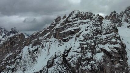 Wall Mural - aerial view of amazing rocky mountains in snow under moody gray clouds, dolomites, italy, 4k