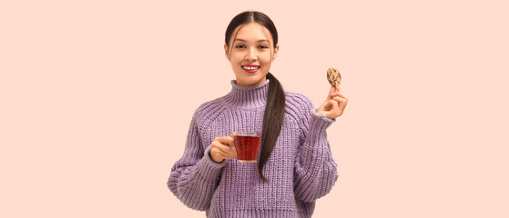 Poster - Beautiful young Asian woman with glass cup of hot tea and sweet cookie on pink background