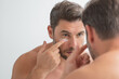 © Volodymyr - Millennial hispanic man looking in mirror, facial skin and stubble. Male beauty care product. Skincare, home spa. Beauty portrait of a beautiful man. Spa model, moisturizing nourishing creme.