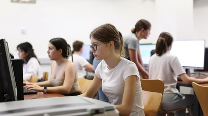 Wall Mural - Side view on focused teenager female student sitting at desk in computer class in library, preparing for exam 