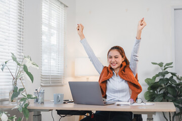 Wall Mural - Cheerful woman celebrating success while working on laptop in bright home office.