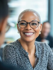 Wall Mural - This is a stock image of a professional woman with short gray hair, wearing glasses and smiling. She appears to be engaged in a conversation with someone out of frame. The background suggests an