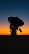 © IbragimovN - Silhouette of satellite dish against vibrant sunset and starlit sky in desert