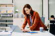 © Nuttapong punna - Confident business expert attractive smiling young woman typing laptop and holding digital tablet on desk