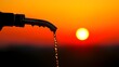 © seksun - A fuel nozzle dispensing fuel, with the sun setting in the background, creating a warm glow