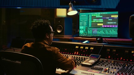 Fototapete - Audio expert counts down for artist singing in vocal booth, recording tracks to edit them after in post production. Producer operates mixing console and buttons or sliders, control room. Camera B.