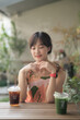 © Jirawatfoto - Asian woman in floral dress enjoys peaceful moment at outdoor cafe with iced coffee and matcha drinks on wooden table
