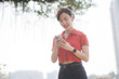 © Jirawatfoto - Asian cheerful woman in red shirt and black jeans smiles while using her smartphone outdoors on sunny day