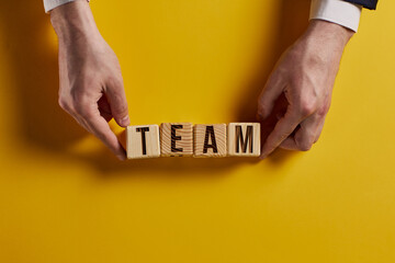 The word TEAM is written on wooden cubes on a yellow table surface.