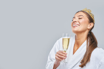 Photo of happy woman in bathrobe over gray background with sparkling wine and crown