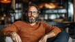 ©  Shomixer - A happy, bearded man casually relaxes in a cozy café, embodying a sense of tranquility and contentment amidst a pleasant atmosphere with warm decor and lighting.