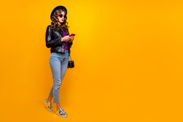 Canvas Print - Full length photo of concentrated girl with curly hairstyle use her smart phone follow subscribe wear black jacket denim jeans clutch isolated over yellow color background