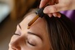 © Thiga.project - a hand applying essential oil to the top part using a dropper bottle on her forehead for healthy and shiny long hair growth concept