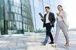 © muse studio - Business professionals walking together and using digital devices in an urban setting during daytime