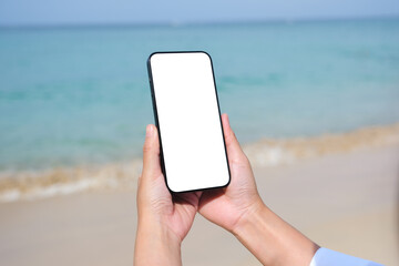 Wall Mural - Mockup image of a woman holding mobile phone with blank desktop screen by the sea