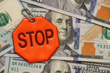 Reflective keychain with text stop lies on hundred dollar bills, business