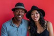 © Markus Schröder - Portrait of a grinning multicultural couple in their 30s donning a classic fedora in solid color backdrop