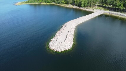 Wall Mural - Drone view of white breakwater on the sea with forested shore in the background on a sunny day