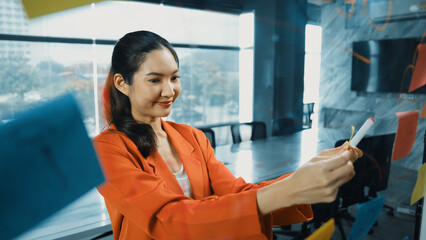 Wall Mural - Happy successful businesswoman gets new idea from sticky note. Businesswoman smiling while standing in front of glass wall with sticky notes contain brainstorming idea, business strategy. Manipulator.