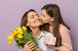 © Butsarakham - mom and daughter A joyful mother receives a kiss from her daughter while holding yellow tulips and a gift, set against a soft purple background.