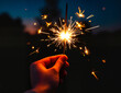 © MyDigitalCraft - Hand holding sparkler against dark background.