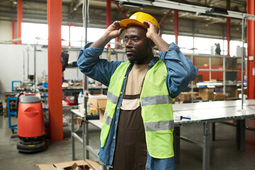 Aufkleber - Young male engineer in overalls, denim shirt and fluorescent jacket putting on safety hardhat before work in warehouse