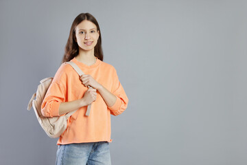 Portrait of smiling teenage girl with backpack on grey background. Space for text