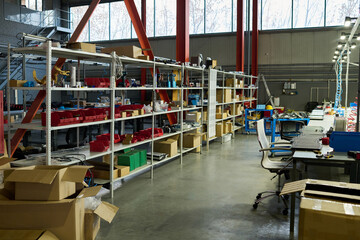 Aufkleber - Wide aisle between tables with electric equipment and shelves with spare parts and packed boxes in spacious workshop