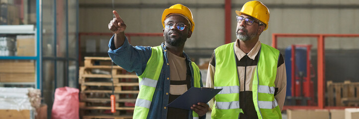 Leinwandbilder - Header of young man in workwear pointing at new industrial equipment while discussing its quality with mature colleague