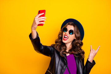 Wall Mural - Heavy metal blogger Party influencer Portrait of funny comic girl make selfie show two fingers horned sign enjoy heavy metal concert wear cap black, outfit isolated over yellow color background