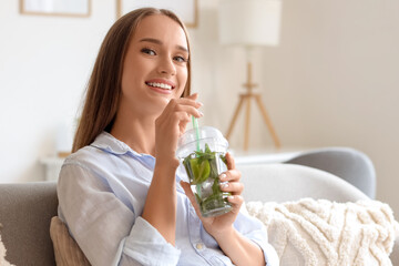 Poster - Beautiful young happy woman with cup of mojito sitting on sofa at home