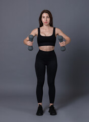 Wall Mural - Woman in sportswear exercising with dumbbells on grey background