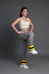 Wall Mural - Woman in sportswear exercising with ankle weights on grey background