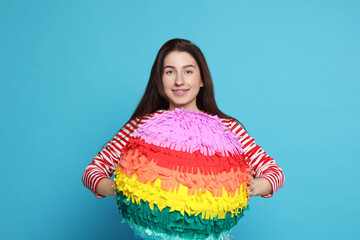 Happy woman with pinata on light blue background