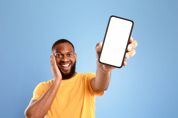 Poster - Check out this cool mobile app. Excited African American man presenting smartphone with empty screen, recommending website or ad on blue studio background, space for mockup. Selective focus