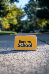 Poster - Back to school sign in yellow, placed on a sidewalk with trees in the background
